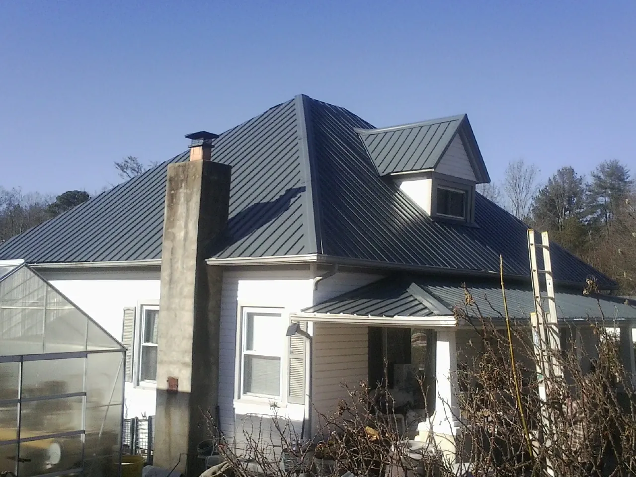 Dark blue standing seam metal roof on a white farmhouse with dormer — Slate & Tile Roof Repair by Roofing Brothers in Eldena