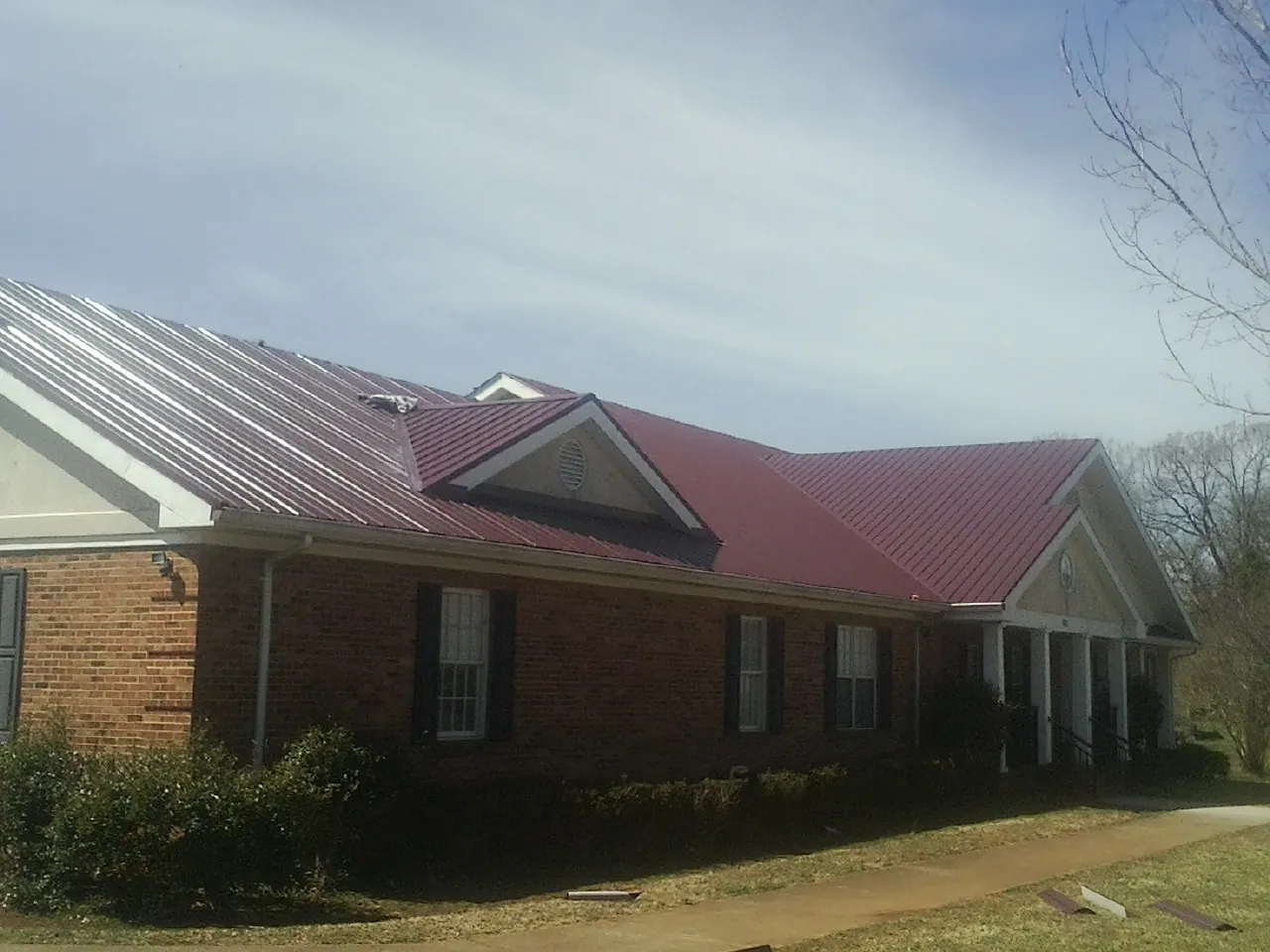 Red metal roof with gabled entries on a long brick building, from a Hail Damage Roof Repair job in Eldena