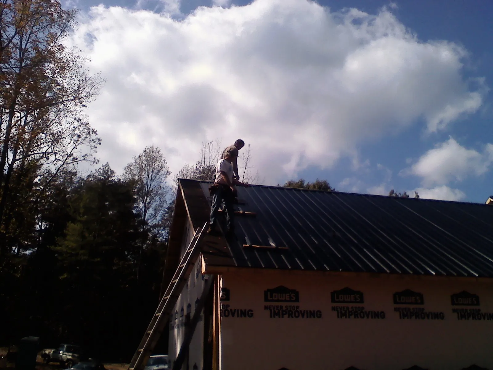 Roofer fastening dark metal panels high against a cloudy sky, from a Roof Inspection job in Eldena